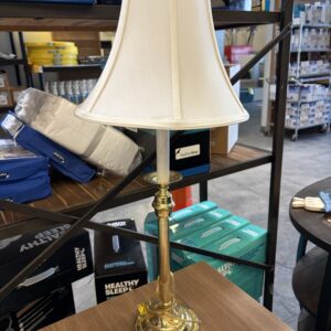 Brass table lamp with white shade on a brown wood table in a store, priced at $3.00.