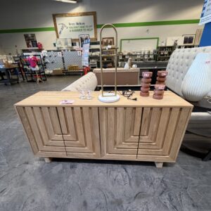 Wooden sideboard with geometric patterns, lamp, stacked candles, and glasses in a furniture store.