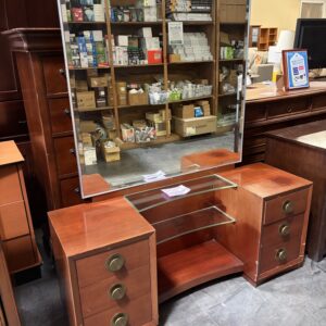 Wooden vanity with a large mirror, glass shelves, and drawers, set in a warehouse with boxes on shelves.