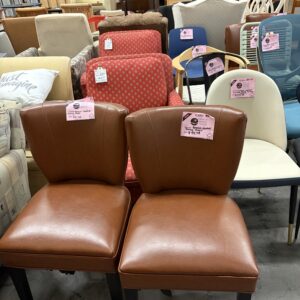 Two brown leather chairs are displayed among various other chairs in a furniture store.