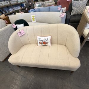 Cream loveseat with a Thankful pillow, displayed in a furniture store with other couches nearby.