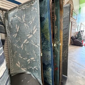 Several large rugs with various patterns, including dragonflies and leaves, displayed upright in a store.