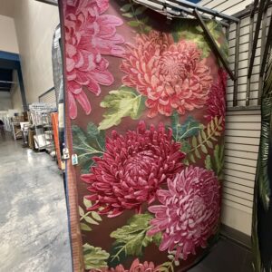 Large rug with pink and red chrysanthemum flowers and green leaves displayed in a store aisle.