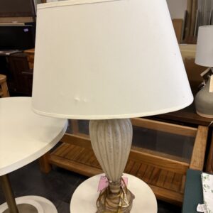 A beige table lamp with a white shade sits on a white round table in a furniture store.