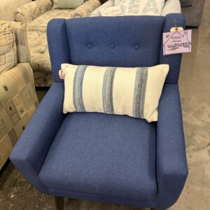 Blue armchair with a white and blue striped pillow, displayed on a concrete floor in a furniture store.