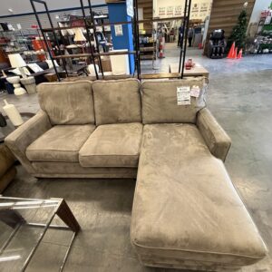 Beige sectional sofa with chaise on display in a furniture store, near a glass coffee table.