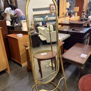 Gold-framed standing mirror surrounded by wooden furniture in a secondhand store.
