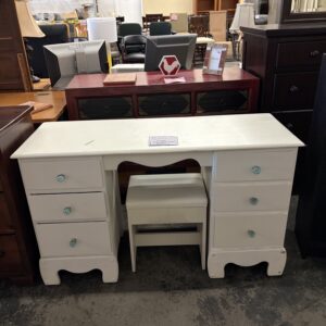 White wooden desk with six drawers and a matching stool, displayed in a furniture store setting.