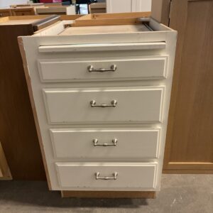 White four-drawer cabinet with metal handles, sitting on a concrete floor among other cabinets.