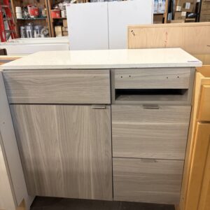 Light wood cabinet with two drawers, a cupboard, and a white countertop in a warehouse setting.