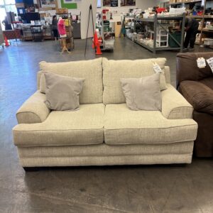 Beige two-seat sofa with two grey throw pillows in a store.