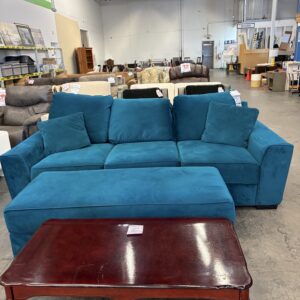 A teal sofa and matching ottoman in front of a dark wood coffee table in a furniture store.