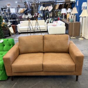 A tan leather two-seater sofa in a furniture showroom.