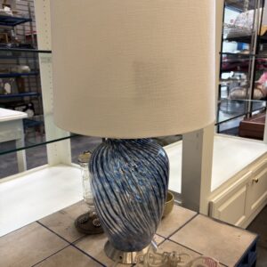 Table lamp with a blue and white swirled glass base and a beige fabric drum shade.
