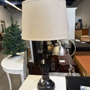 Table lamp with a black cage base and a beige fabric drum shade.