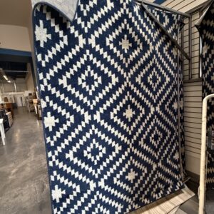 Navy blue rug with a white geometric diamond pattern hanging on a display rack.