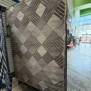 A beige and brown area rug with a large-scale diamond pattern hanging in a store.
